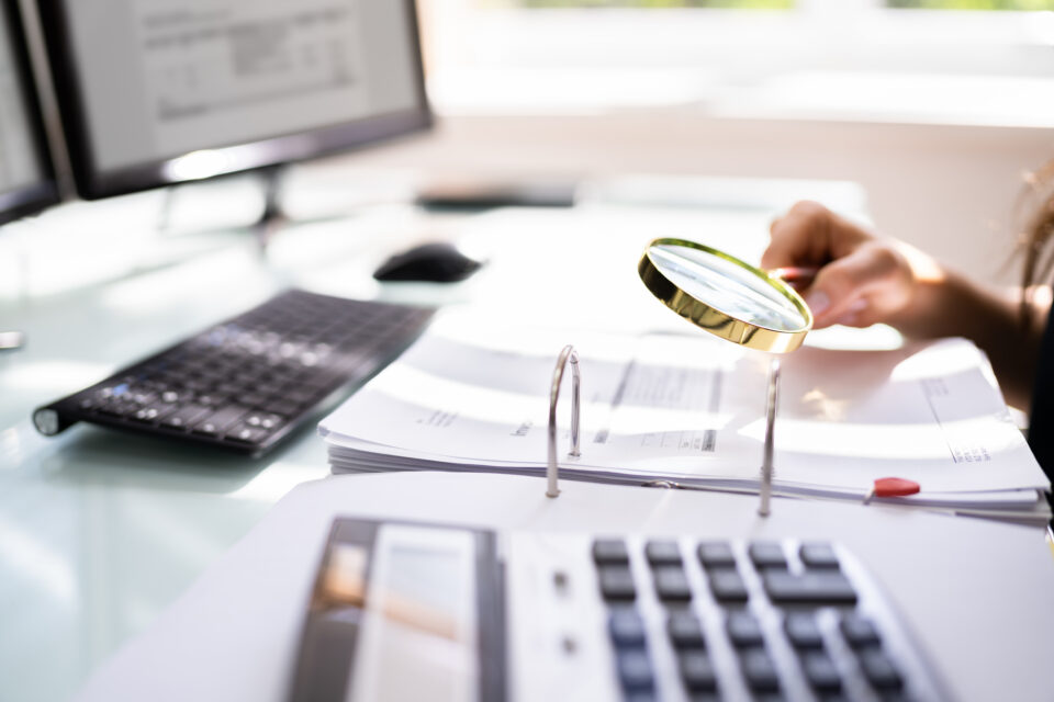 Person Examining Paper Using Magnifier Glass. Tax Fraud Investigation